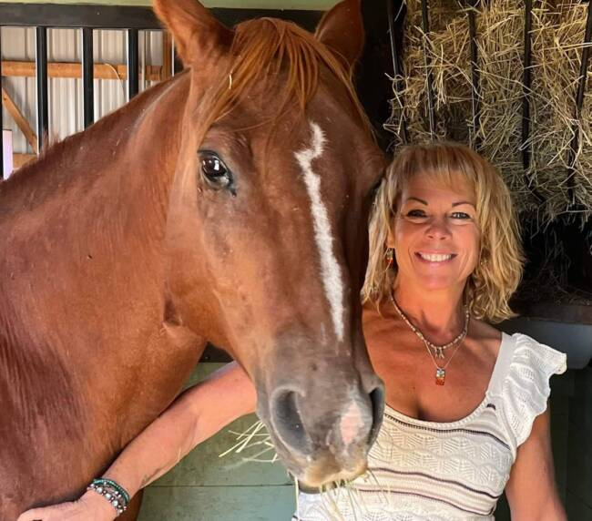 Woman smiling beside a brown horse inside a rustic barn at Three Willows Ranch in Bayfield Colorado