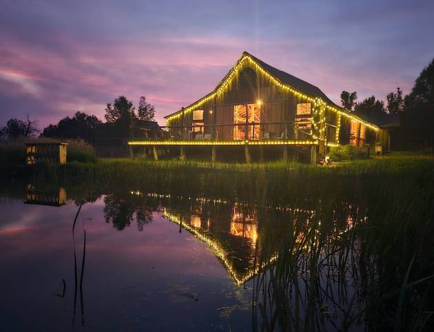 Rustic barn at Three Willows Ranch glowing with evening lights reflected on the water in Colorado