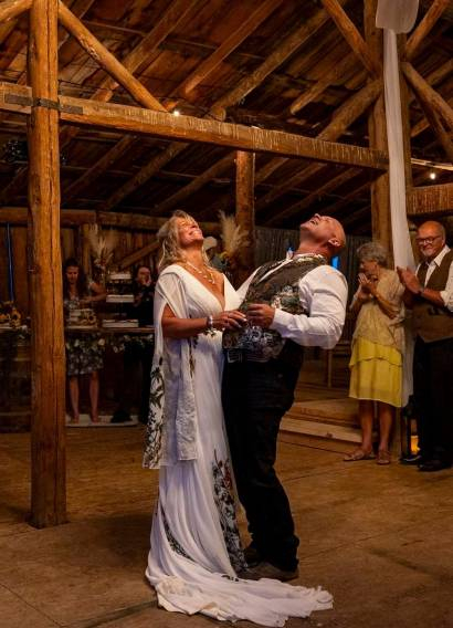 Bride and groom laughing during their first dance inside a rustic wooden barn at a Colorado ranch wedding venue.