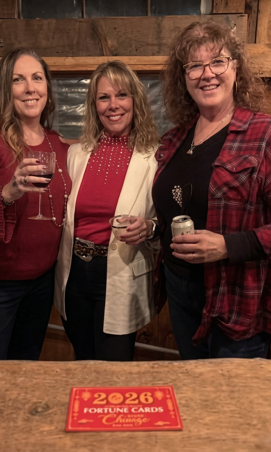 Three women smiling and holding drinks while celebrating together at a rustic barn bar during an event at Three Willows Ranch in Colorado.