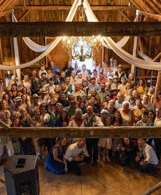 Wedding guests gathered inside a historic wooden barn reception space with chandelier and draped fabric at a rustic Colorado ranch venue.