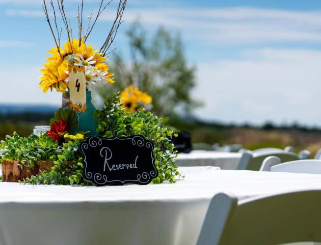 Rustic wedding table centerpiece with sunflowers, greenery, and reserved sign at outdoor ranch reception.